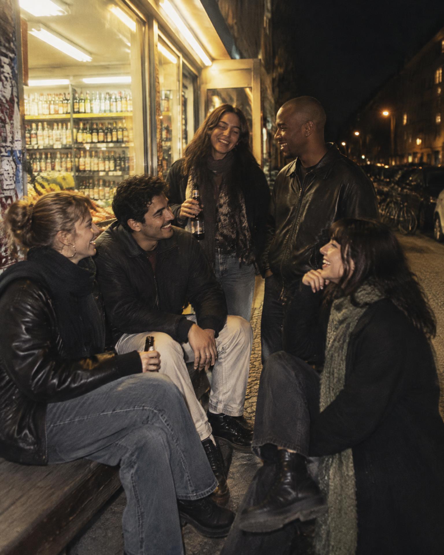 Freunde lachen nachts vor einem Berliner Späti